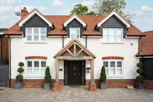 Two-story modern house in Colchester with traditional architecture, striking red tile roof, and manicured shrubs.